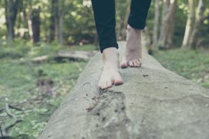 Das Bild zeigt nackte Fäße balancierend auf einem Baumstamm im Wald.