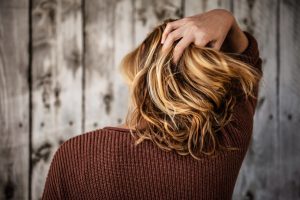 Das Bild zeigt eine junge Frau mit blonden, schulterlangen Haaren von hinten, wie sie sich in die Haare greift.